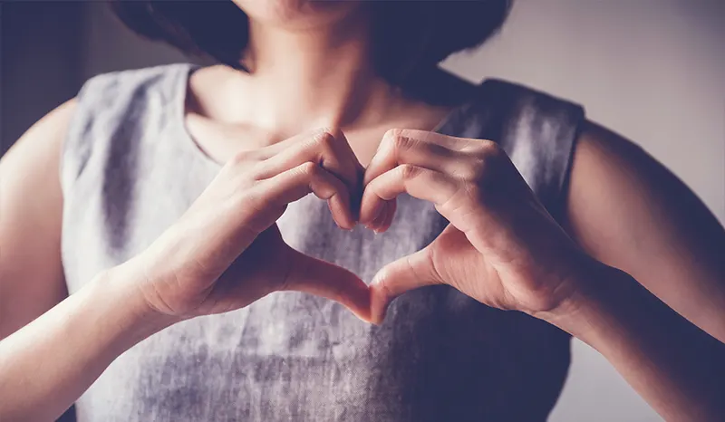 A young girl making a shape of a heart with her hands.