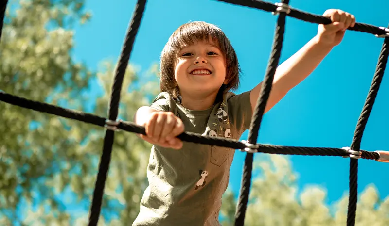 a smiling young boy climbing a rope ladder